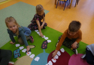 Trójka dzieci przelicza szablony mapy Polski ułożone w rzędzie, odwracają trzeci z kolej.